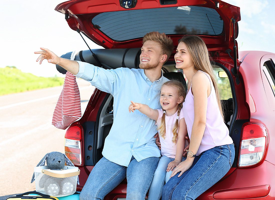 Personal Insurance - Family Sits at the Back of Their Red Car During a Trip on a Sunny Day